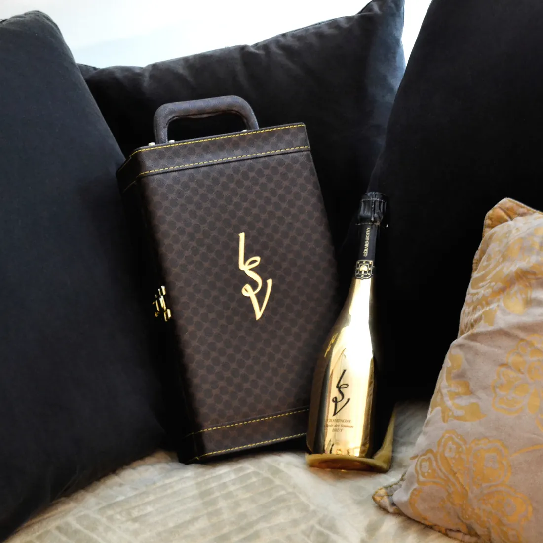 Coffret en cuir monogrammé LSV posé à côté d'une bouteille de champagne dorée