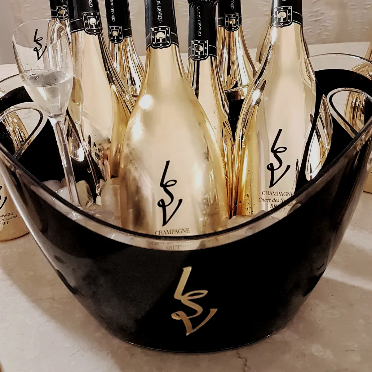 Vasque noire au monogramme LSV remplie de bouteilles de champagne dorées et de flûtes
